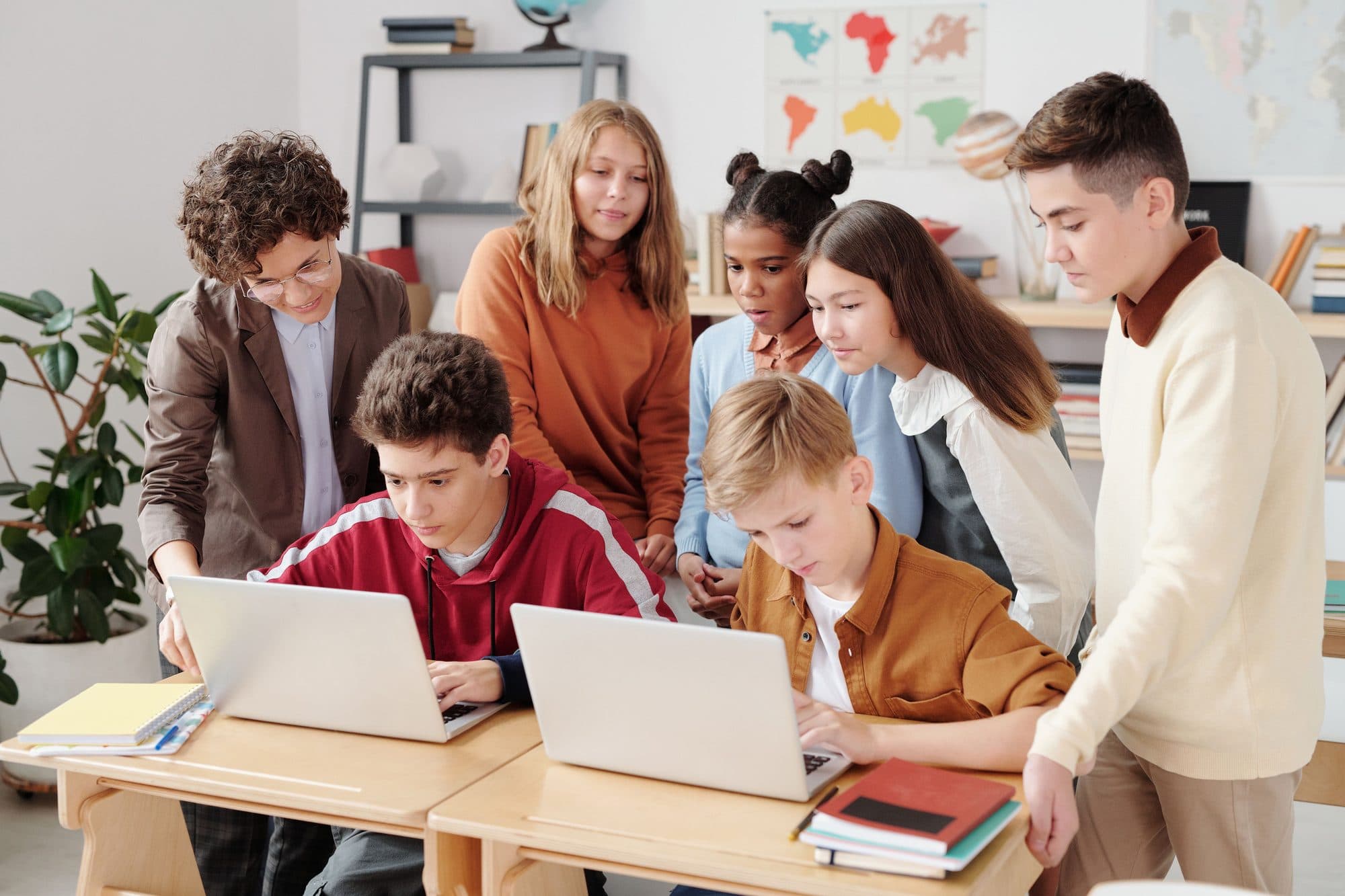 A teacher leaning in to help a group of students working on laptops, individual attention close at hand